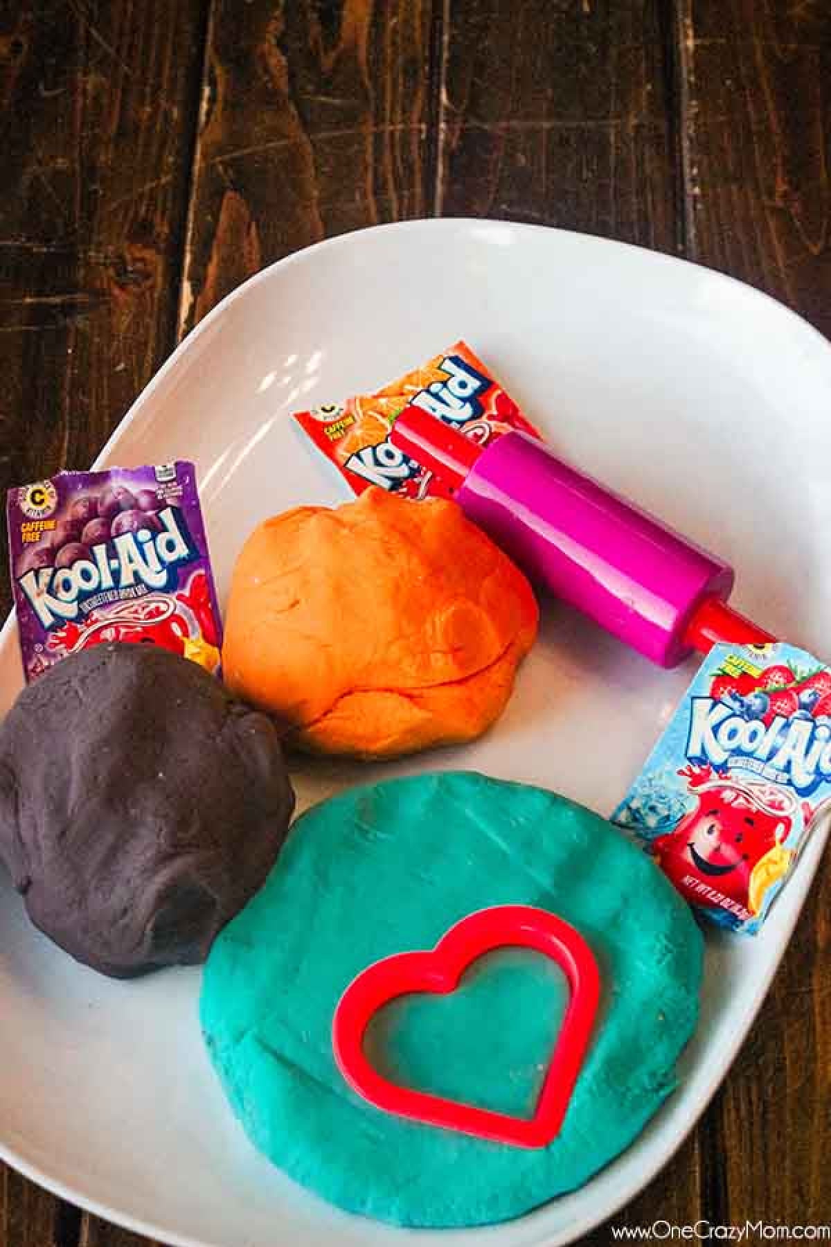 Make this easy Kool Aid Playdough for a fun activity for your kids. Homemade playdough with kool aid is simple to make and the colors are so vibrant. Different colors of kool aid playdough on a plate.