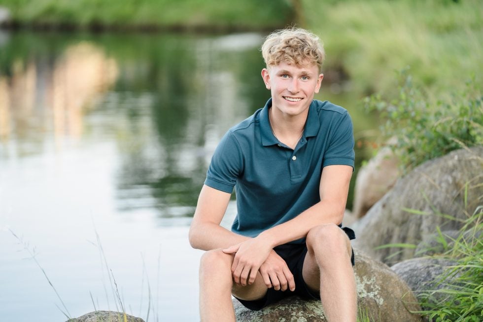 Boy sitting in front of pond.